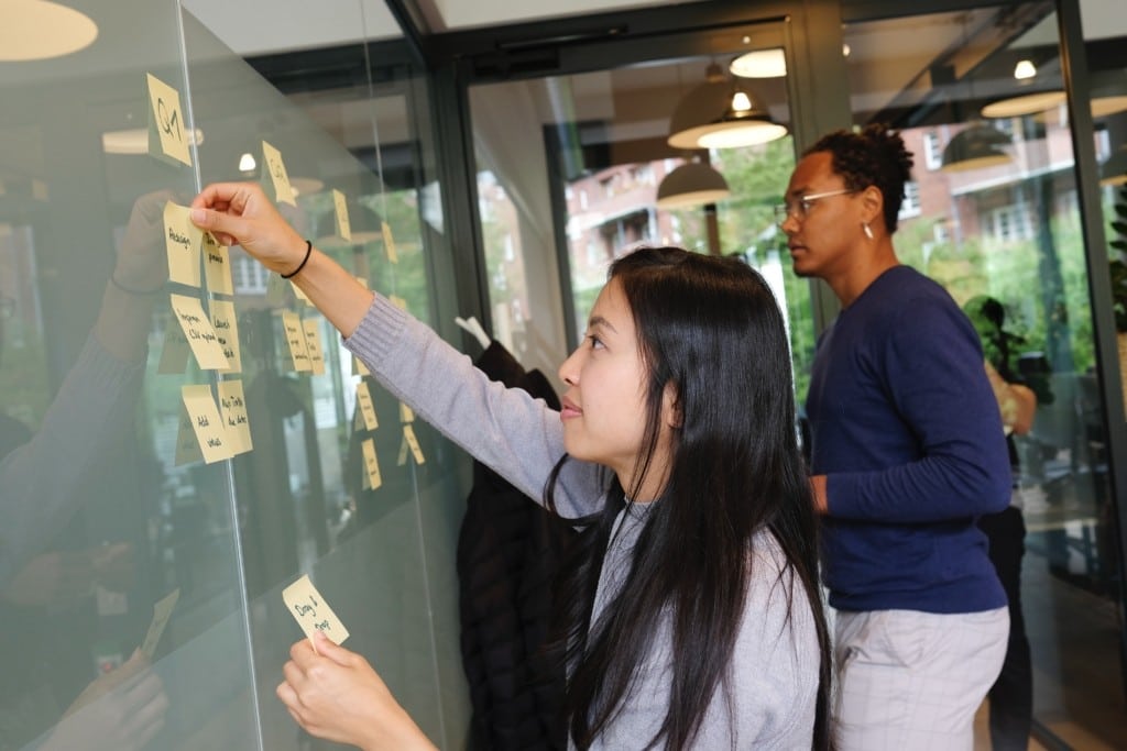 Two people putting post-it notes on a whiteboard to prioritize next tasks
